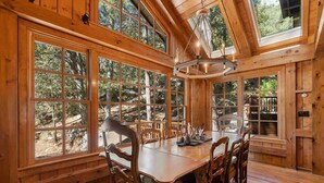 Ein Esszimmer aus Holz mit großen Fenstern, einer Kristallleuchtre und Blick auf den Wald.