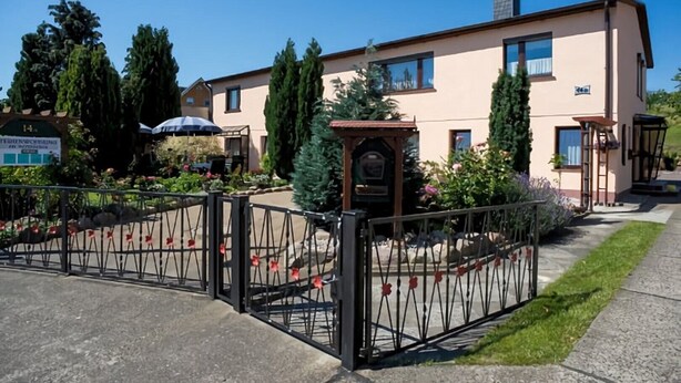 Ein zweistöckiges Gebäude mit einer beigen Fassade, einem verschlossenen Eingang und einem kleinen Garten mit Blumen und einem Brunnen.
