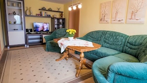 Ein Wohnzimmer mit einem grünen Sofa, einem Holztisch mit Blumenvase, einem Fernseher und Regalen mit Dekoration.