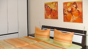 Ein Schlafzimmer mit einem Bett, zwei Kissen, einem Nachttisch und zwei an der Wand hängenden Schmetterlingsbildern.