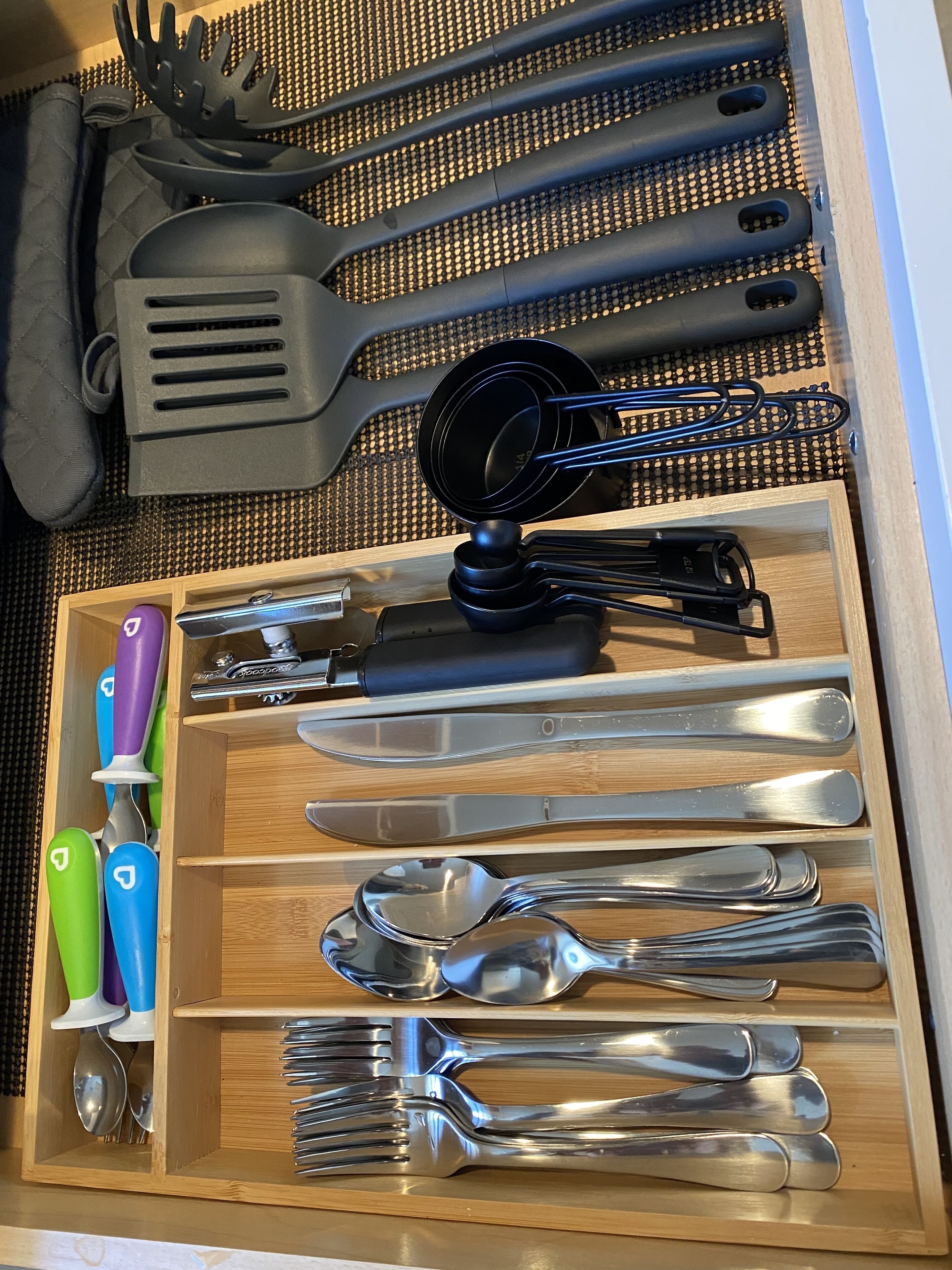 A drawer with neatly organized kitchen utensils including spoons, forks, knives, and a grater.