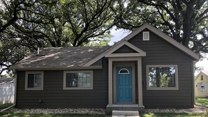 Una casa pequeña de un solo piso con fachada marrón oscuro, puerta delantera azul y un porche pequeño.