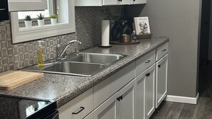 Cocina moderna con armarios blancos, encimeras de granito, pileta de acero inoxidable y una ventana con persianas.