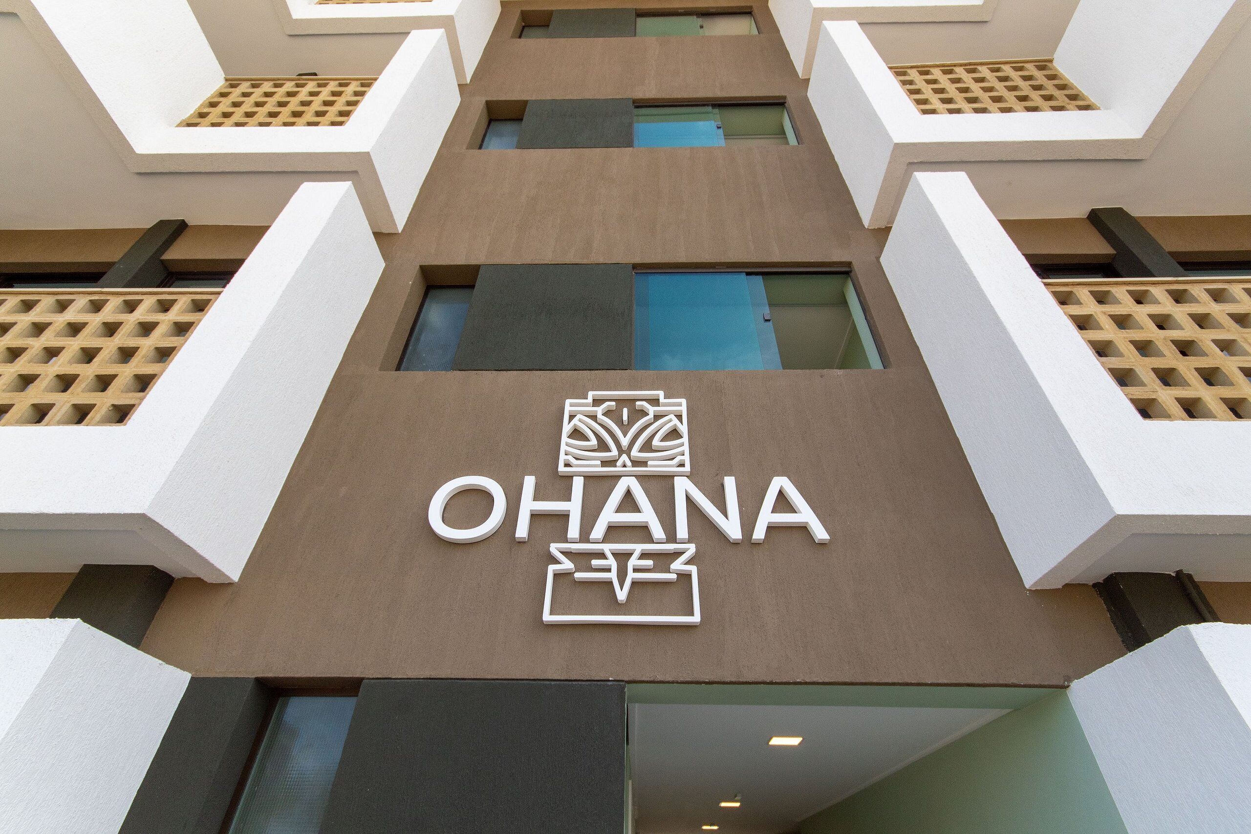 Um edifício moderno com fachada geométrica, com o nome "OHANA" em destaque ao centro.