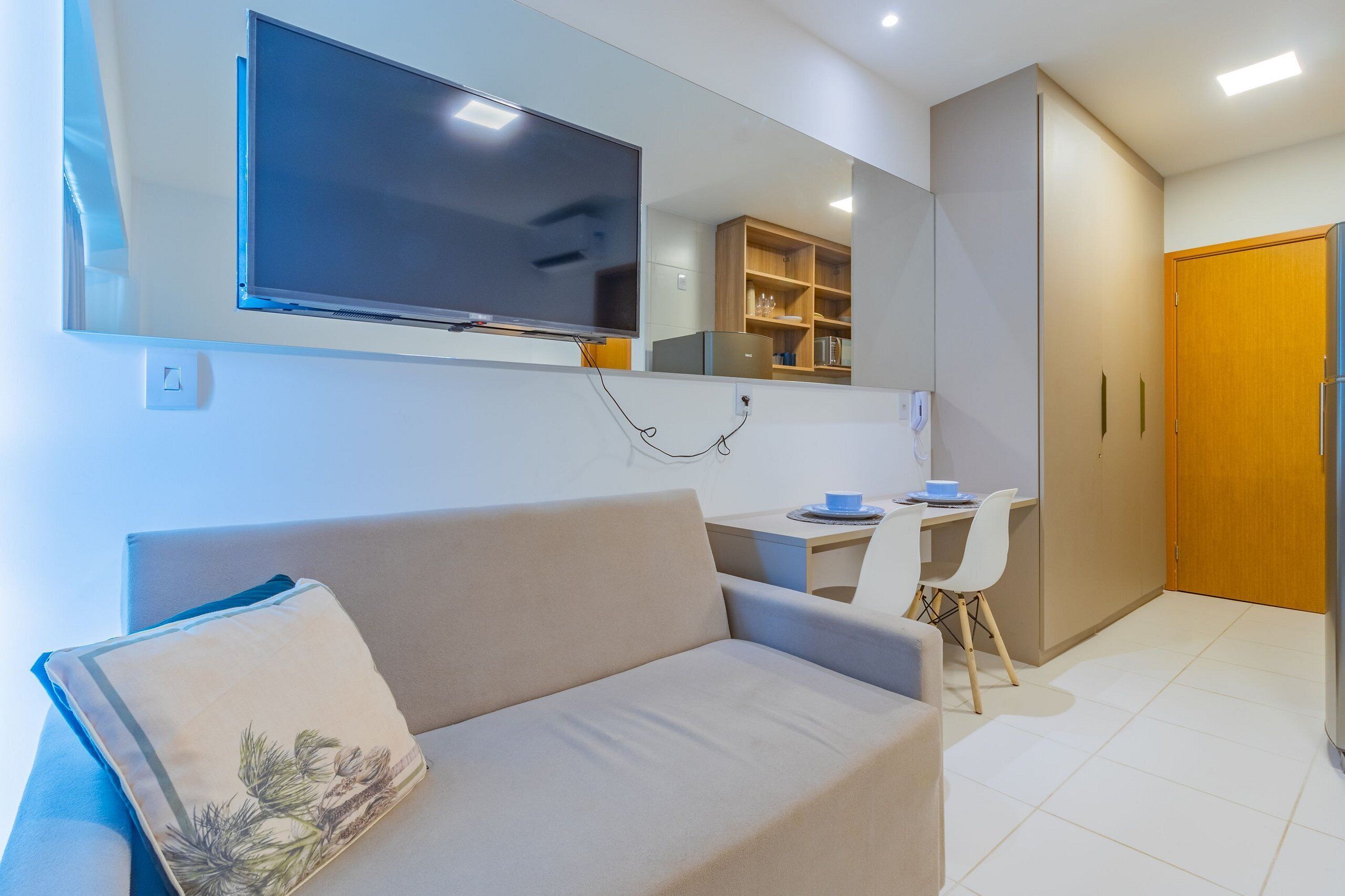 Un salon moderne comprenant un canapé, un téléviseur à écran plat fixé au mur, un bureau avec une chaise et un meuble en bois.