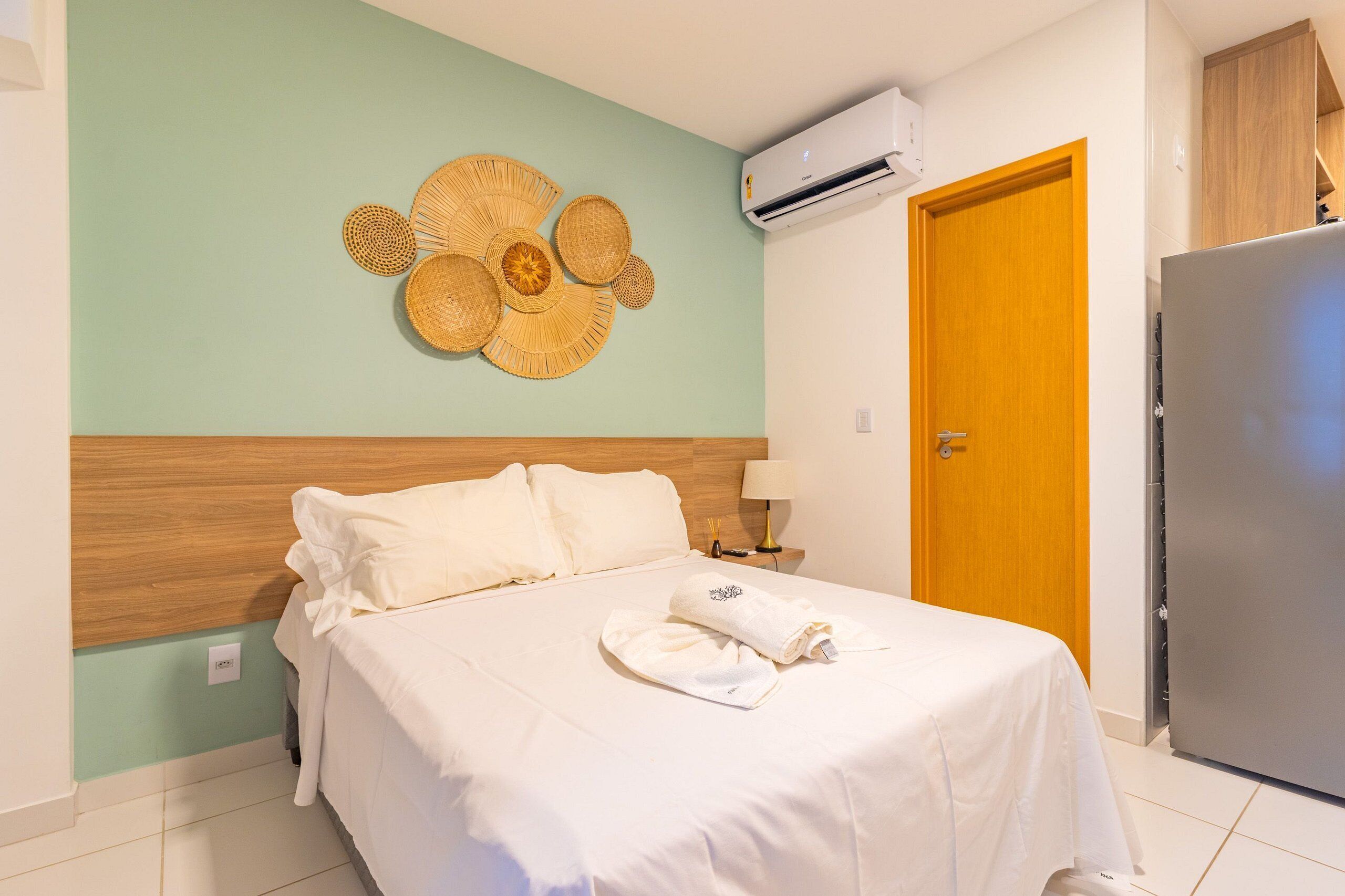 Une chambre d’hôtel équipée d’un lit, d’un climatiseur fixé au mur, d’une porte en bois et d’un réfrigérateur.