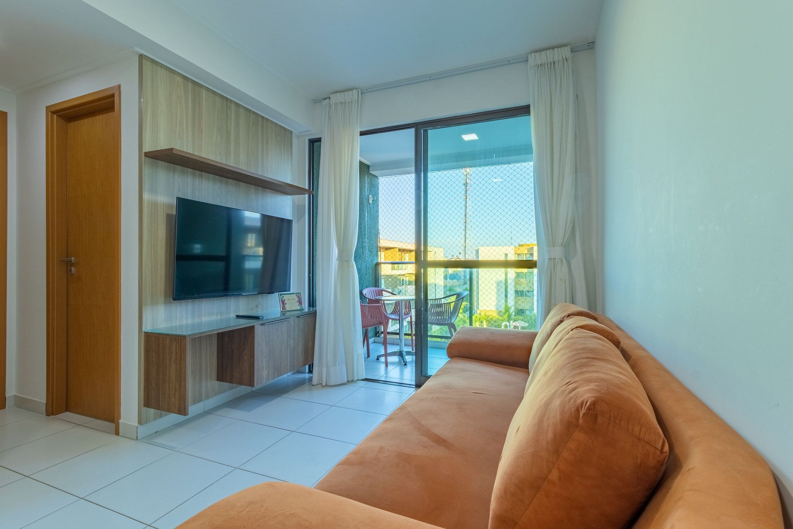 Una sala moderna con sofá, televisión y balcón con mesa y sillas.