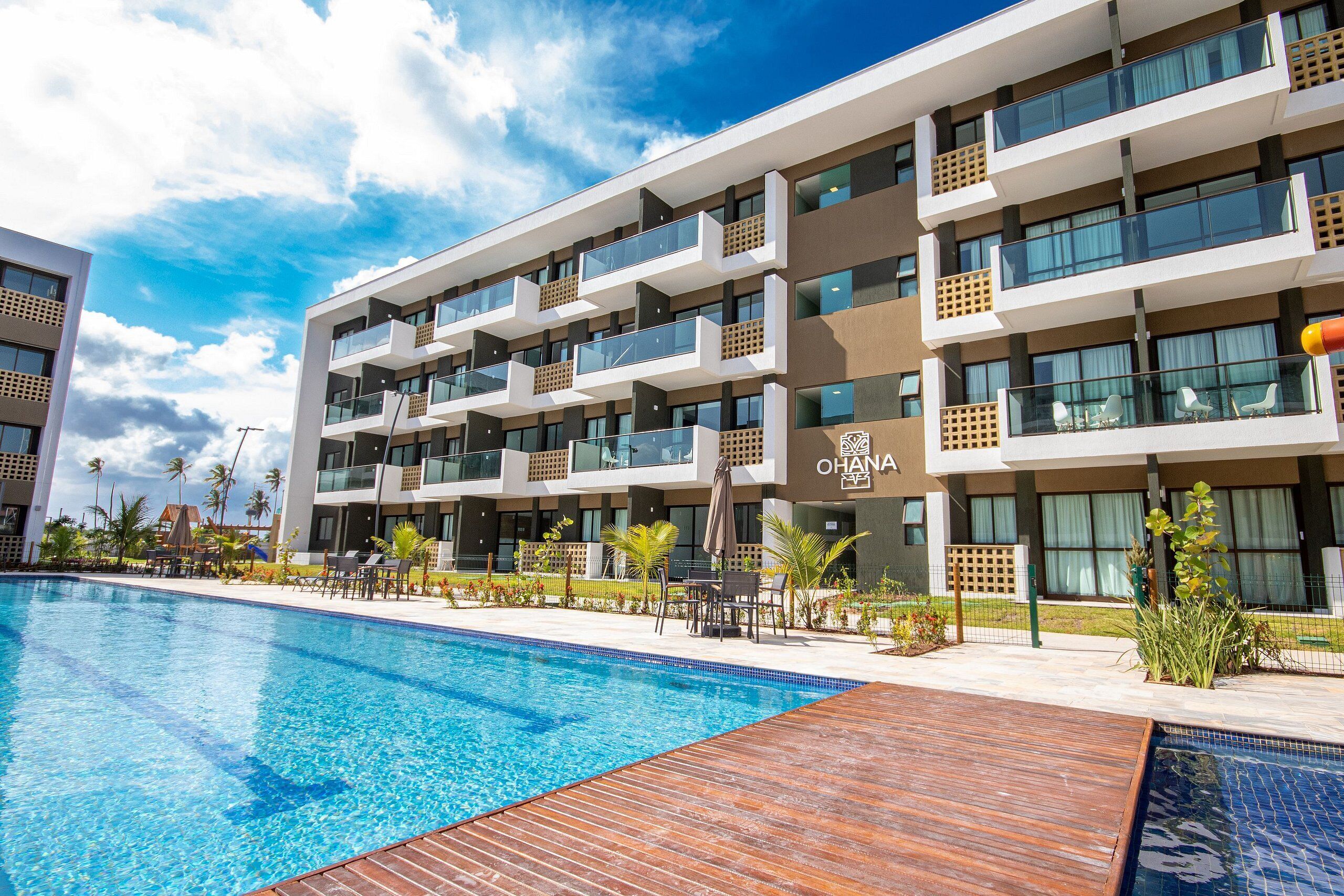 A modern hotel with a swimming pool, multiple balconies, and a clear sky.