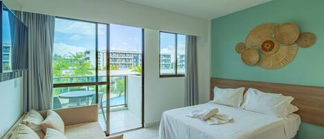 Ein Hotelzimmer mit Bett, Sofa, einem Balkon mit Blick auf Gebäude und Grünflächen sowie einer Wanddekoration.