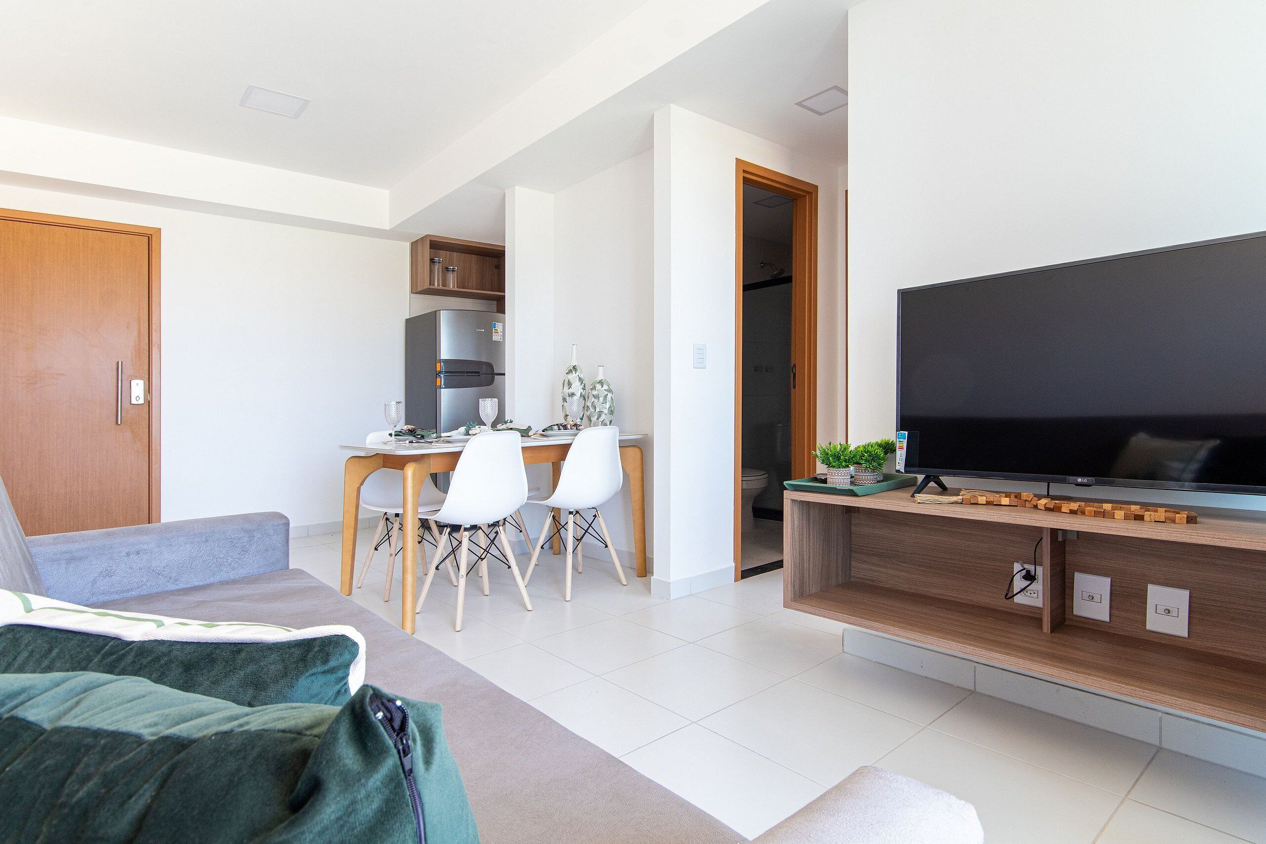 Ein modernes Wohnzimmer mit einer Couch, einem Fernseher, einem Essbereich mit Stühlen und einer Küche im Hintergrund.