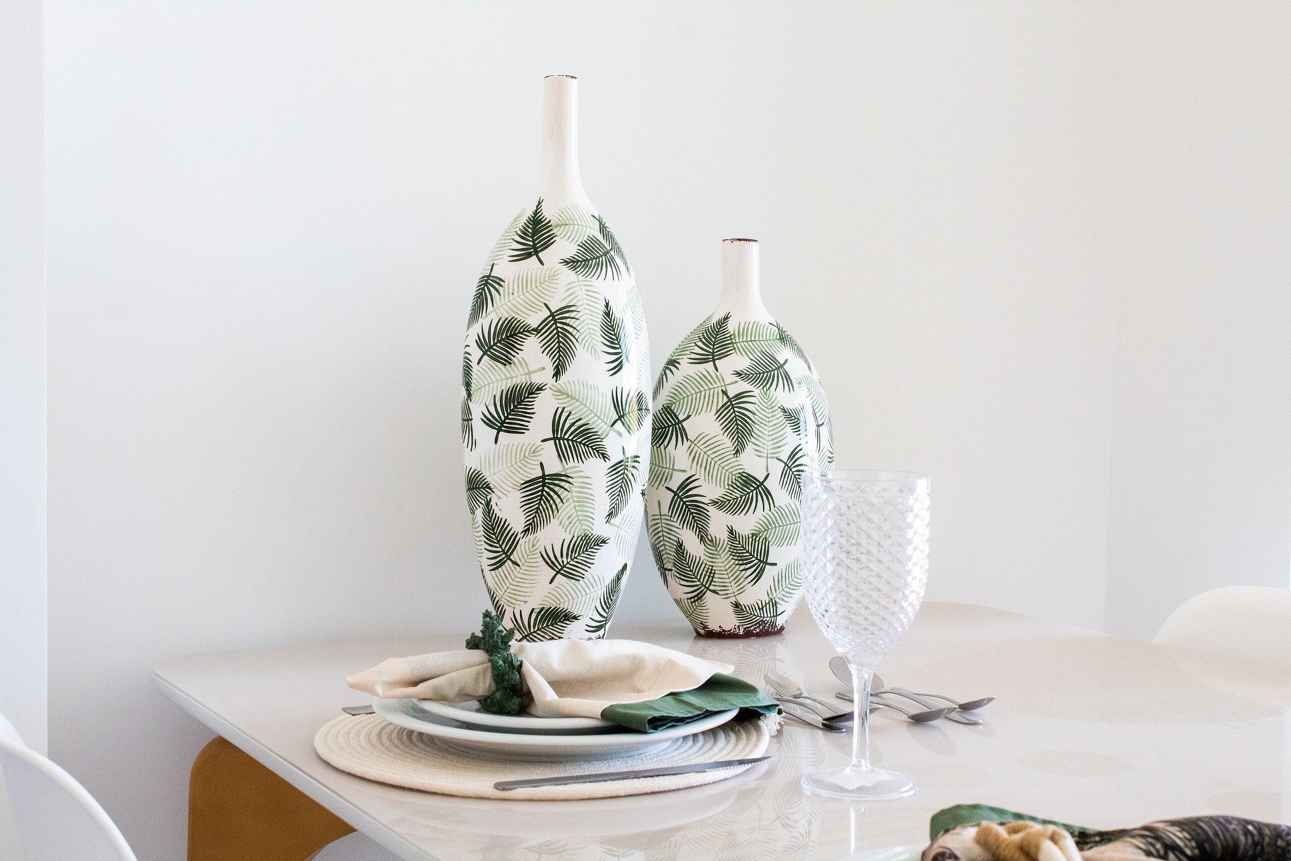 A table with two patterned vases, a glass, and a folded napkin.