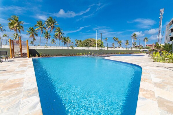 Piscina com água azul cristalina, rodeada por palmeiras e um deck revestido de azulejos.