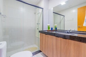 Une salle de bain moderne avec une douche à parois de verre, un meuble-lavabo en bois doté d’un plan de travail noir et un grand miroir.