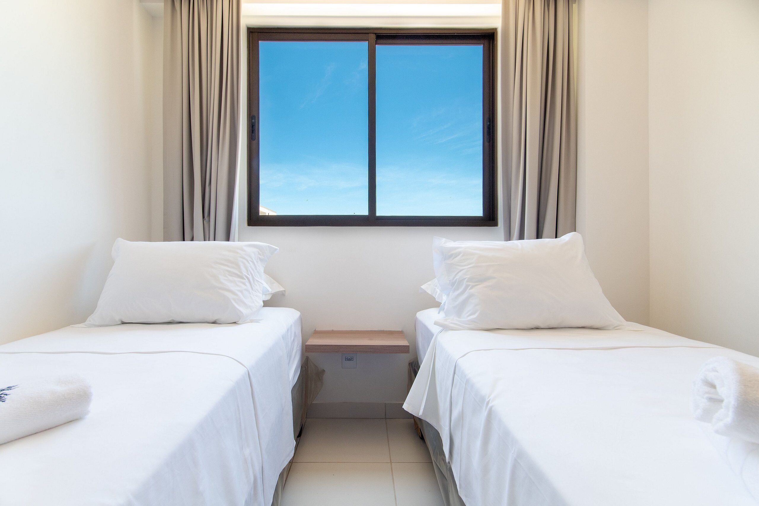 A twin room with two beds, a window with curtains, and a small bedside table.