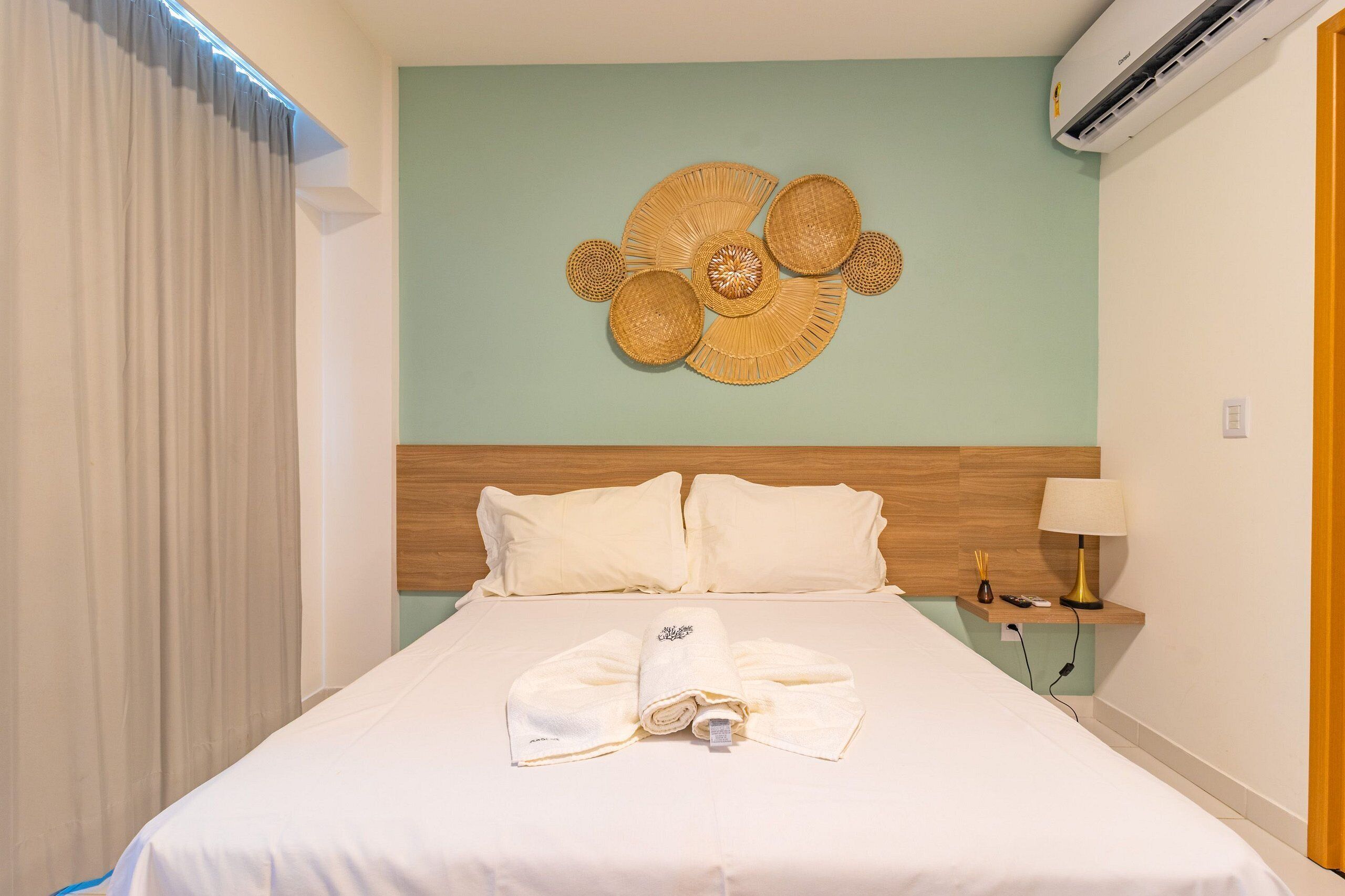 Una habitación de hotel con cama, aire acondicionado de pared, lámpara de noche y un adorno en la pared.