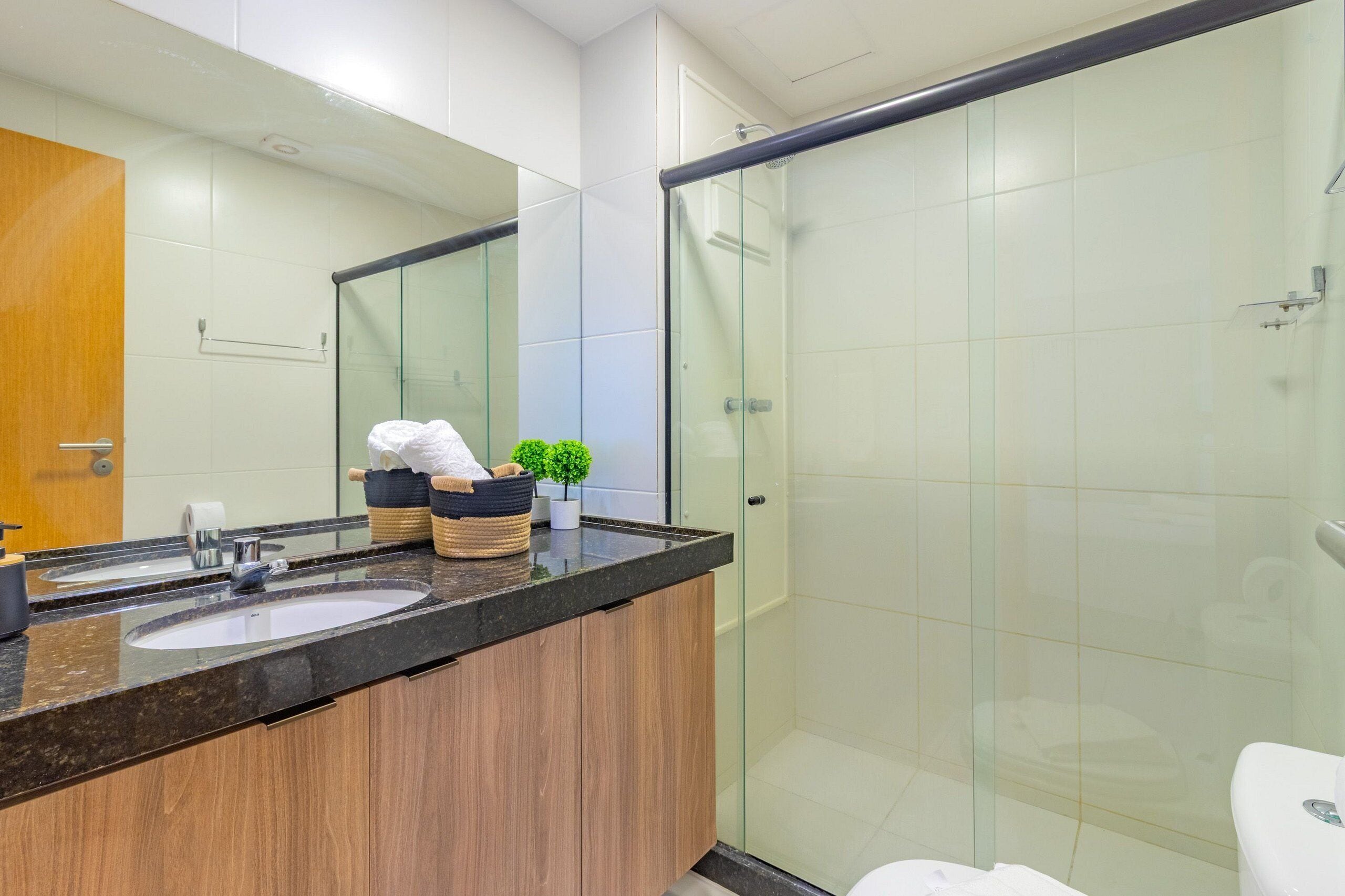 A modern bathroom with two sinks, a glass shower enclosure, and a wooden vanity.