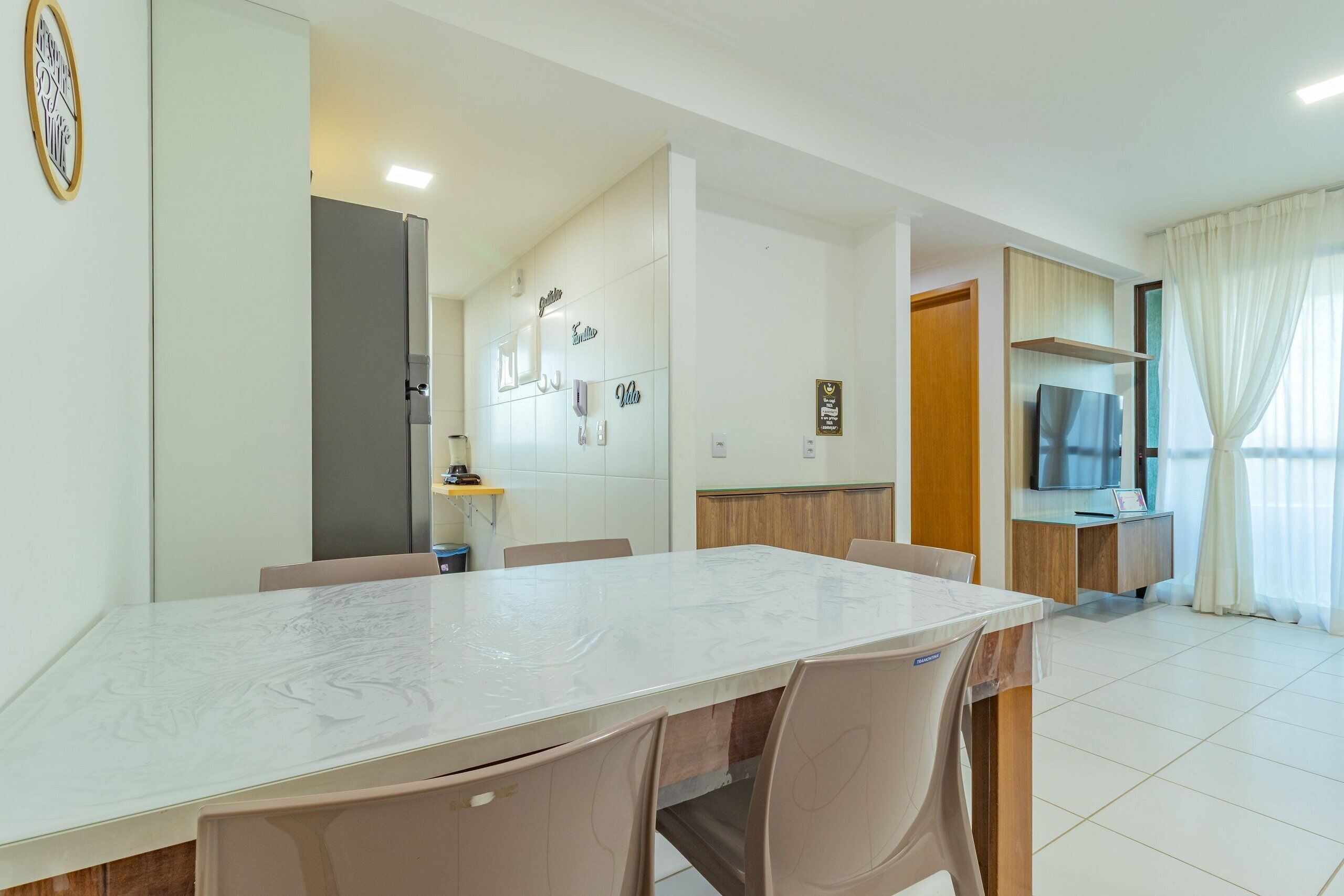 Une chambre d’hôtel moderne avec une table à manger en marbre, des chaises beiges, un téléviseur et un meuble en bois.