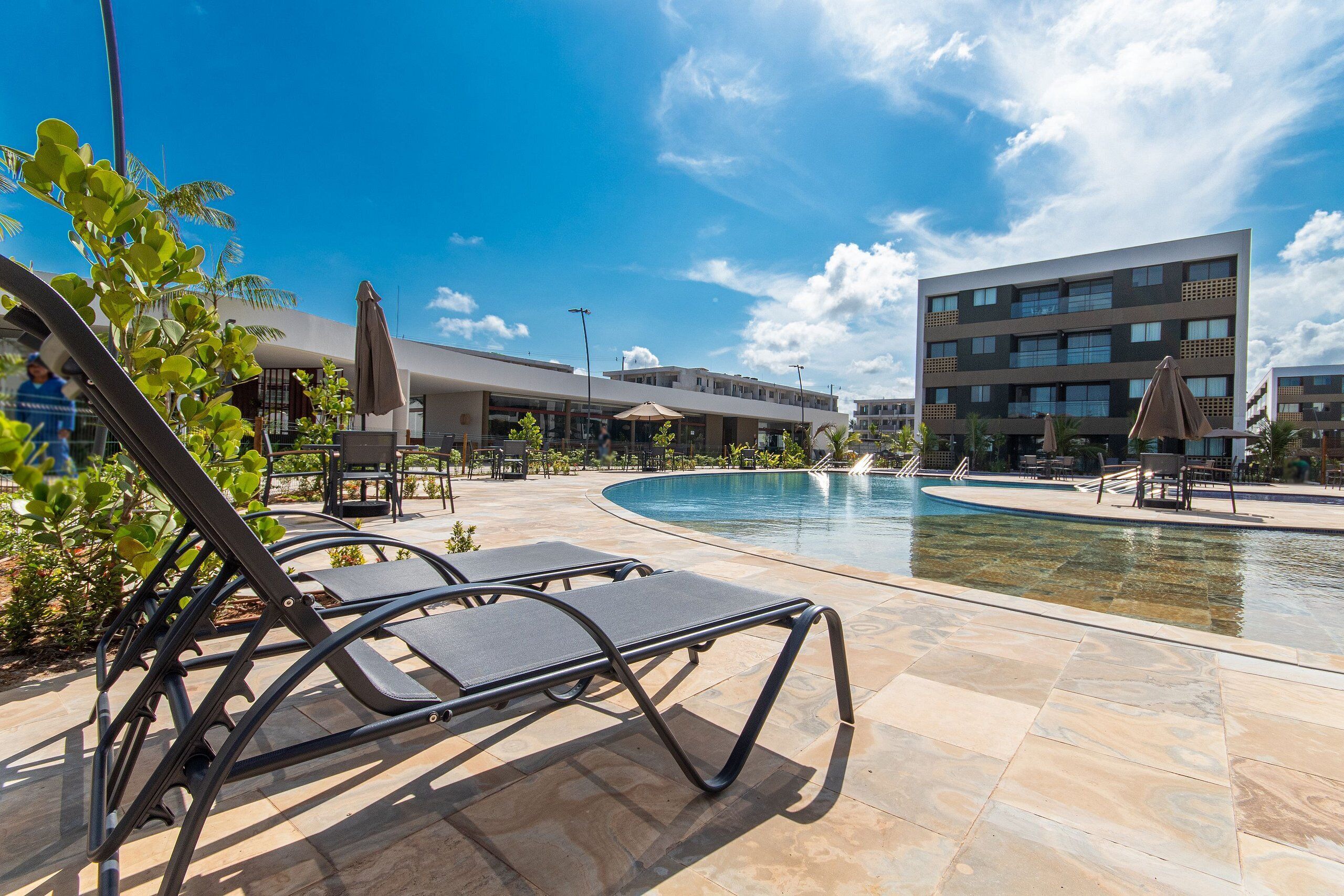 A poolside area with lounge chairs, a swimming pool, and a modern building with multiple balconies.