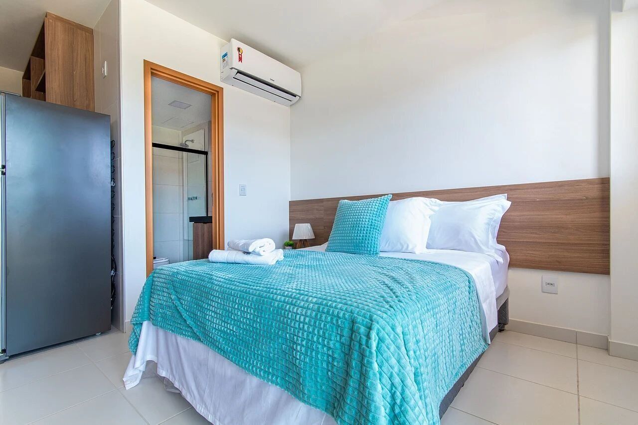 A hotel room with a bed, a wardrobe, and an air conditioning unit.