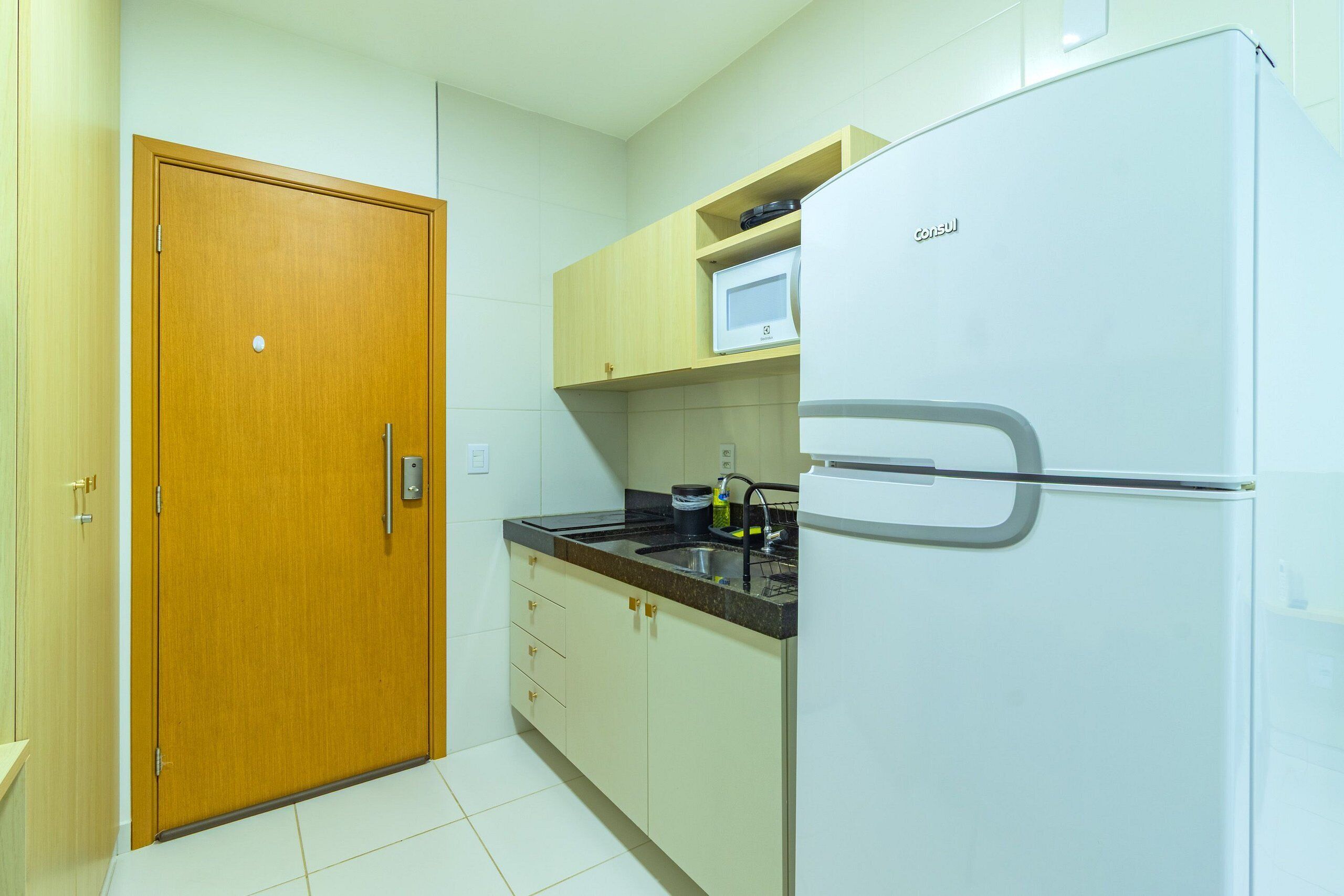 A kitchen with a refrigerator, microwave, sink, and wooden cabinets.