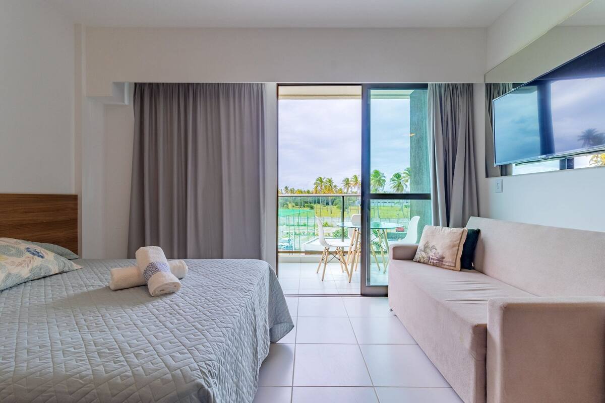 Une chambre d’hôtel avec un lit, un canapé, une télévision et un balcon offrant une vue sur les palmiers.