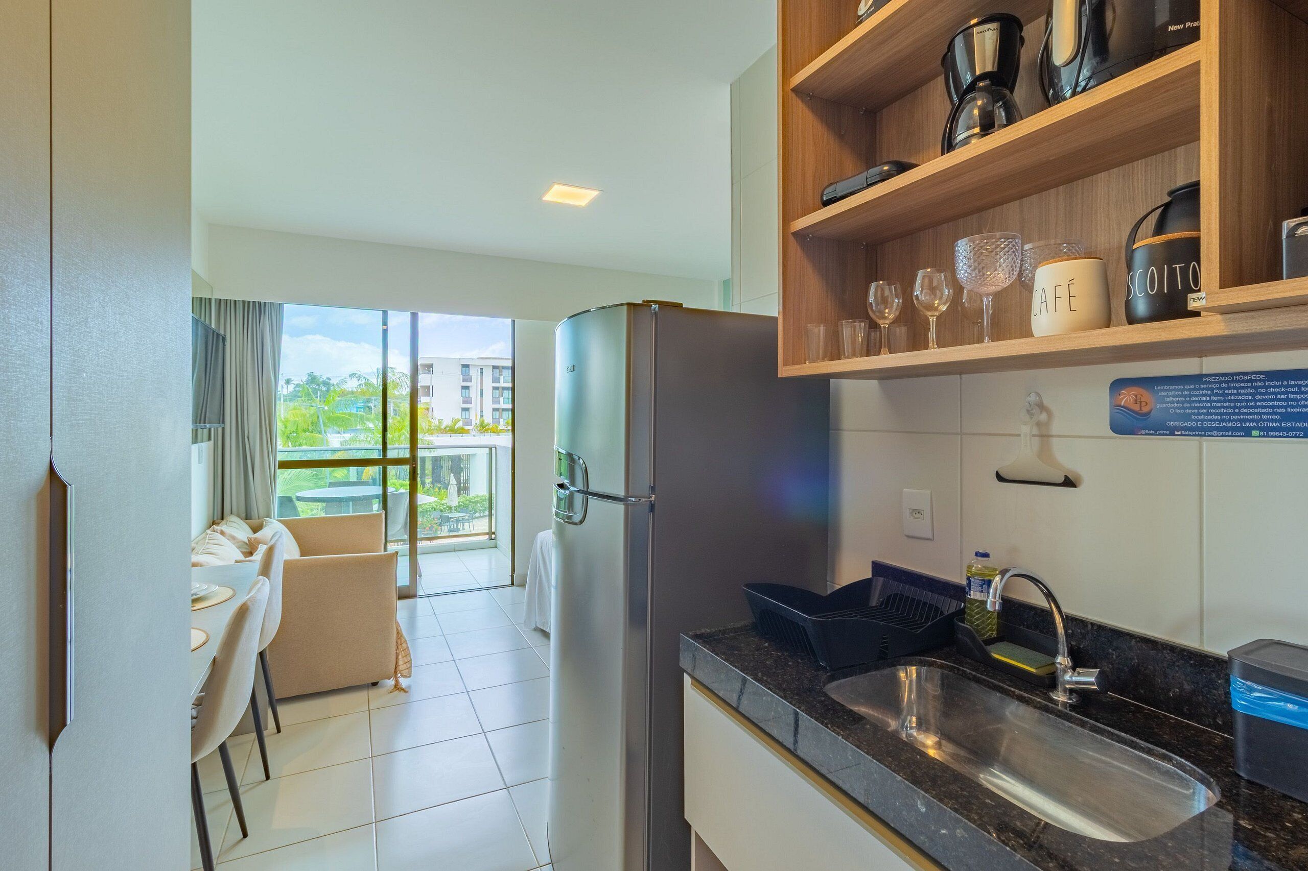 A modern kitchen with a built-in refrigerator, a wooden shelf with kitchenware, a sink, and a dining area with a table and chairs.