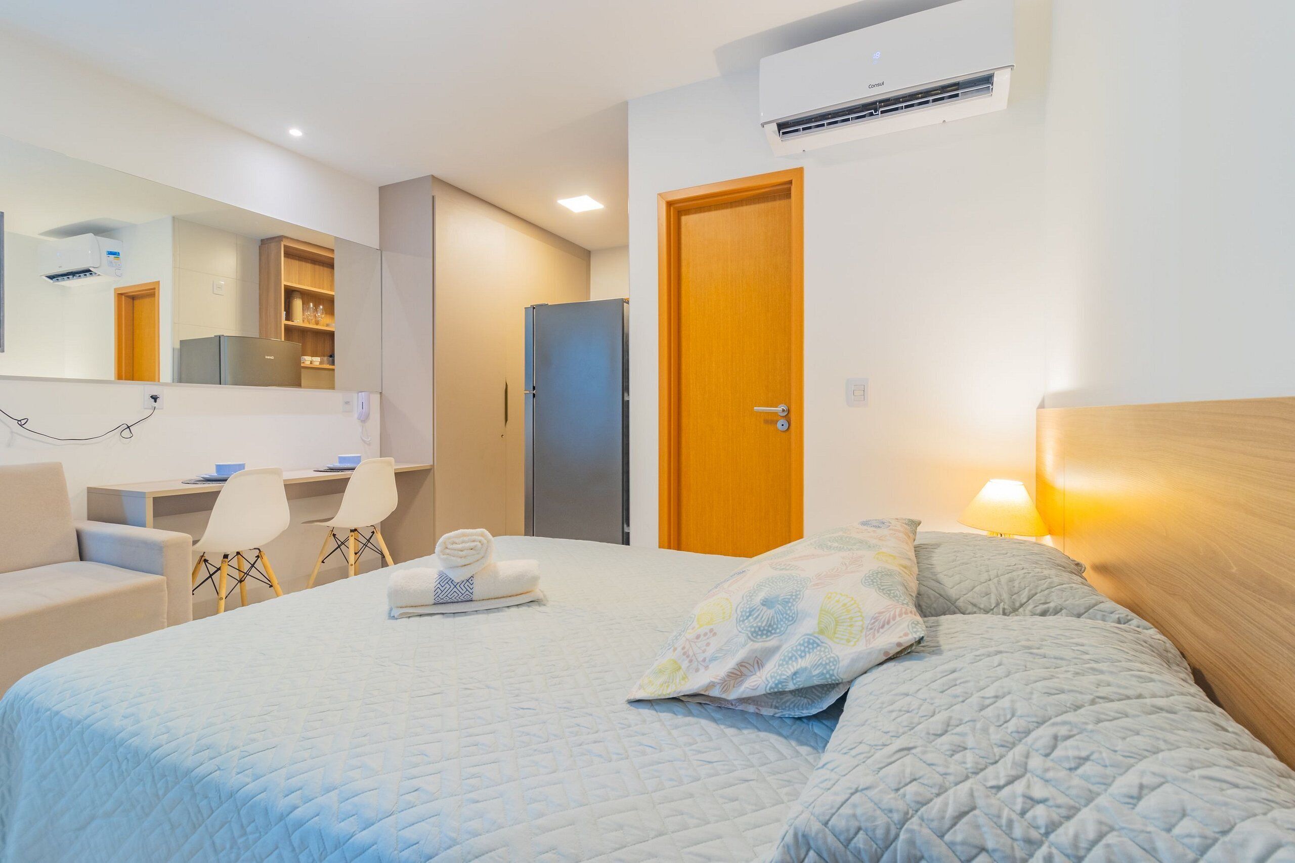 A hotel room with a bed, a desk, a chair, a wardrobe, and an air conditioning unit.
