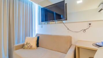 Habitación de hotel con sofá, televisión instalada en la pared, una mesita y una ventana con cortinas.