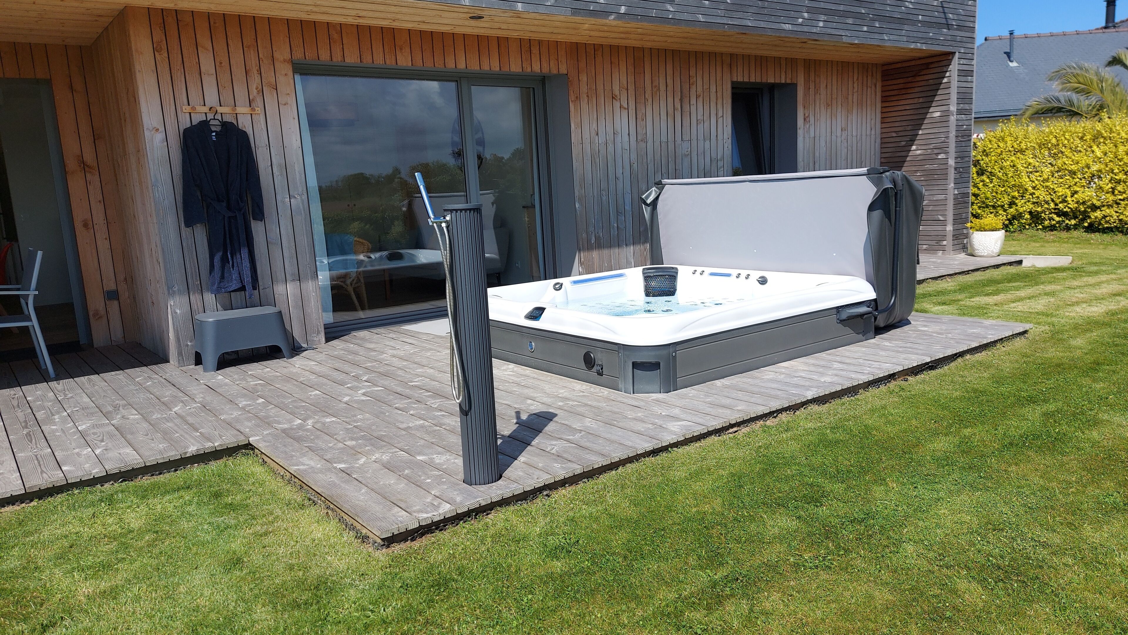 A hot tub on a wooden deck with a glass door leading to a room.