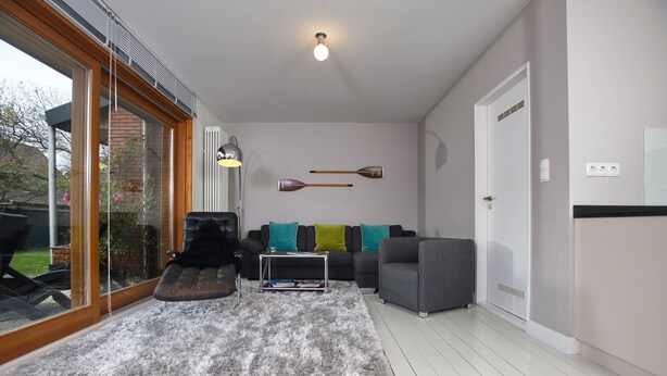 Ein modernes Wohnzimmer mit grauem Sofa, einem Couchtisch und einem großen Fenster mit Jalousien.