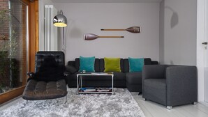 Ein modernes Wohnzimmer mit einem Ledersessel, einem grauen Sofa, einem kleinen Tisch und zwei dekorativen Schlägern an der Wand.