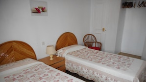 A bedroom with two single beds, a nightstand with a lamp, a chair, and a door.