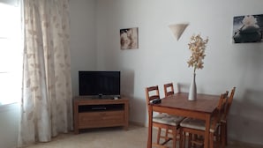 A dining area with a wooden table and chairs, a television on a wooden stand, a vase with flowers, and artwork on the walls.