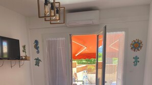 Un salon comprenant un canapé, un téléviseur, une petite table et une porte-fenêtre coulissante donnant sur une terrasse extérieure.