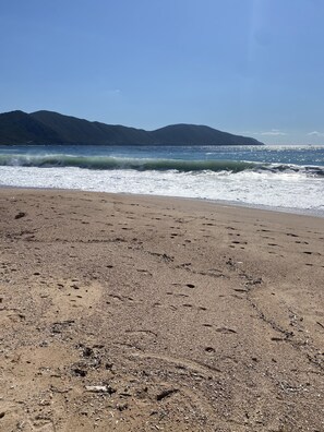 A beach with footprints in the sand and waves crashing onto the shore.