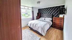 Ein Schlafzimmer mit Bett, Holzkommode und einem fenster mit Vorhängen.