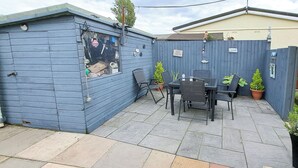 Eine blaue Gartenhütte mit Fenster, eine Terrasse mit Tisch und Stühlen sowie ein eingezäunter Garten.
