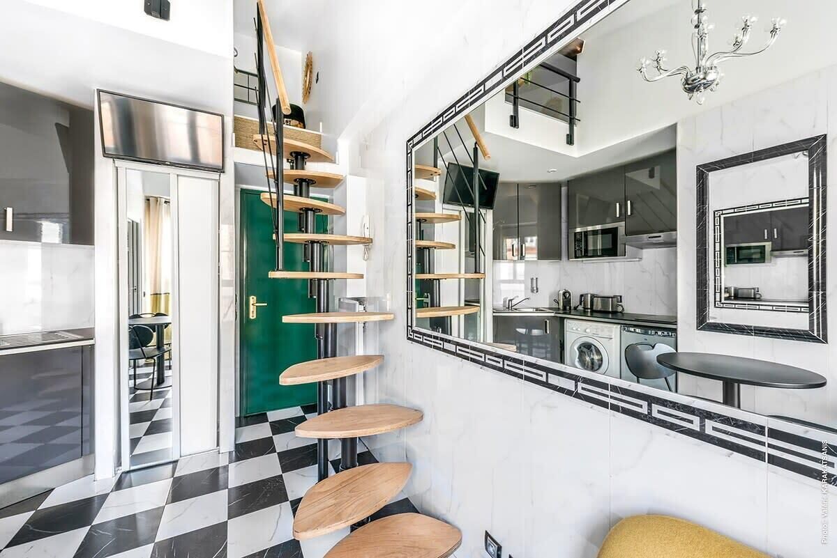 Eine moderne Küche mit einem schwarz-weißen Schachbrettfußboden, einer Wendeltreppe mit Holzstufen und einem großen Spiegel, der die Küche reflektiert.