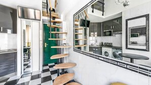 A modern kitchen with a black and white checkered floor, a spiral staircase with wooden steps, and a large mirror reflecting the kitchen. - Studio Colisee - Champs Elysees by B'Your Home (Paris)