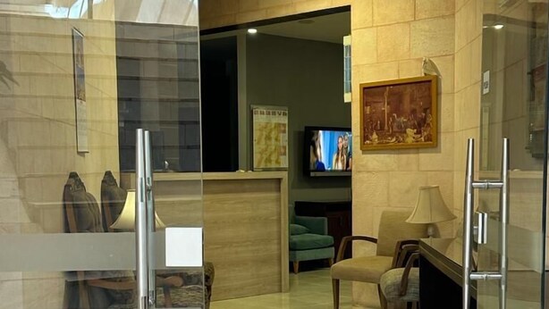 A modern hotel lobby with a glass partition, a reception desk, a television, and seating area. - Petra town check-Inn (Wadi Musa)