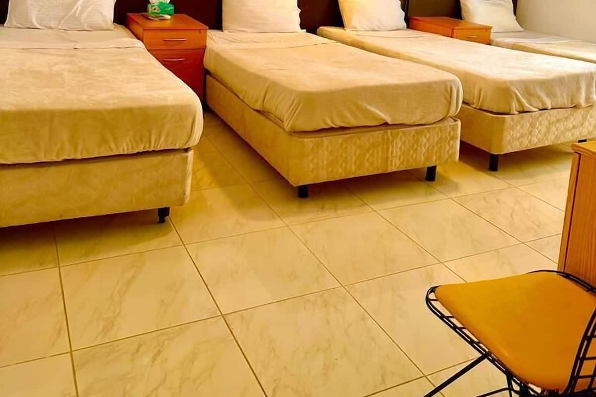 A hotel room with four single beds, a small table, two nightstands, a chair, and a wall-mounted air conditioner.