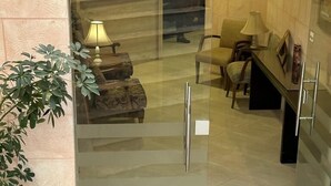 A hotel entrance with a glass door, a potted plant, and a seating area with a lamp and chairs inside. - Petra town check-Inn (Wadi Musa)