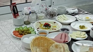 A table set with various dishes, including bread, cheese, and olives, in a room with a view of buildings through a window. - Petra town check-Inn (Wadi Musa)