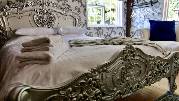 Una cama con dosel metálico decorativo, ropa de cama blanca y toallas dobladas.