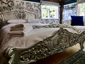 Una cama con dosel metálico decorativo, ropa de cama blanca y toallas dobladas.