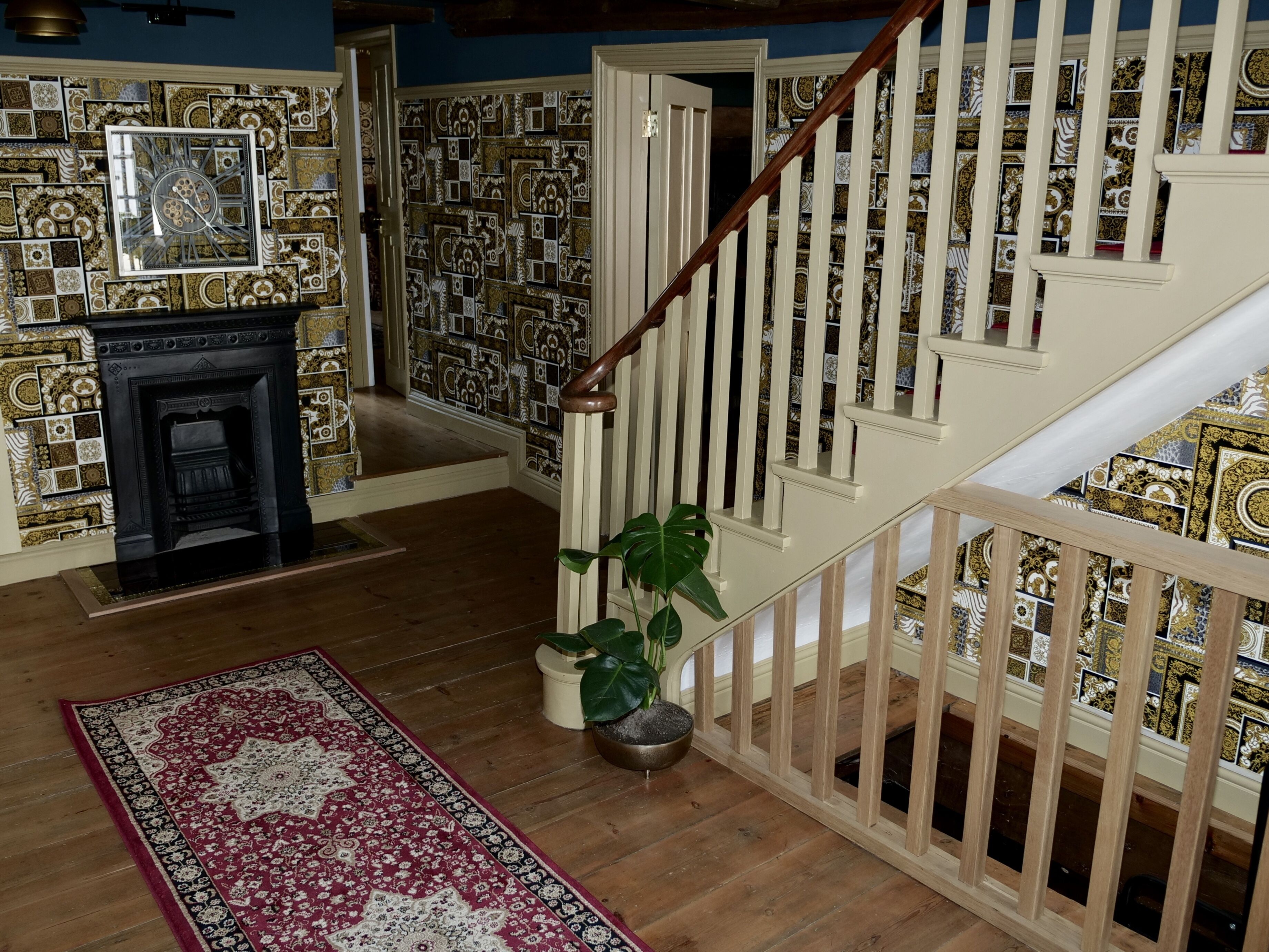 A staircase with a wooden handrail and white balusters, leading to a room with patterned walls and a fireplace.