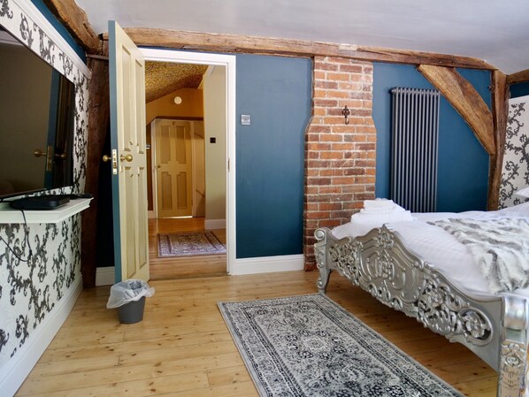 Un dormitorio con cama, cómoda, espejo, radiador y puerta que da a otra habitación.