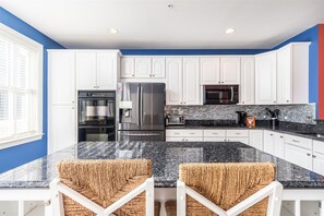 A kitchen with white cabinets, a granite countertop, and a stainless steel refrigerator. - Mini Weeks Stays Available Sunset Island 45 Sunset (Ocean City)