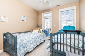 Une chambre à coucher avec un lit, un berceau, une fenêtre avec des stores et une porte.