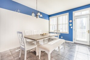 A dining area with a wooden table, white chairs, a bench, and a chandelier.